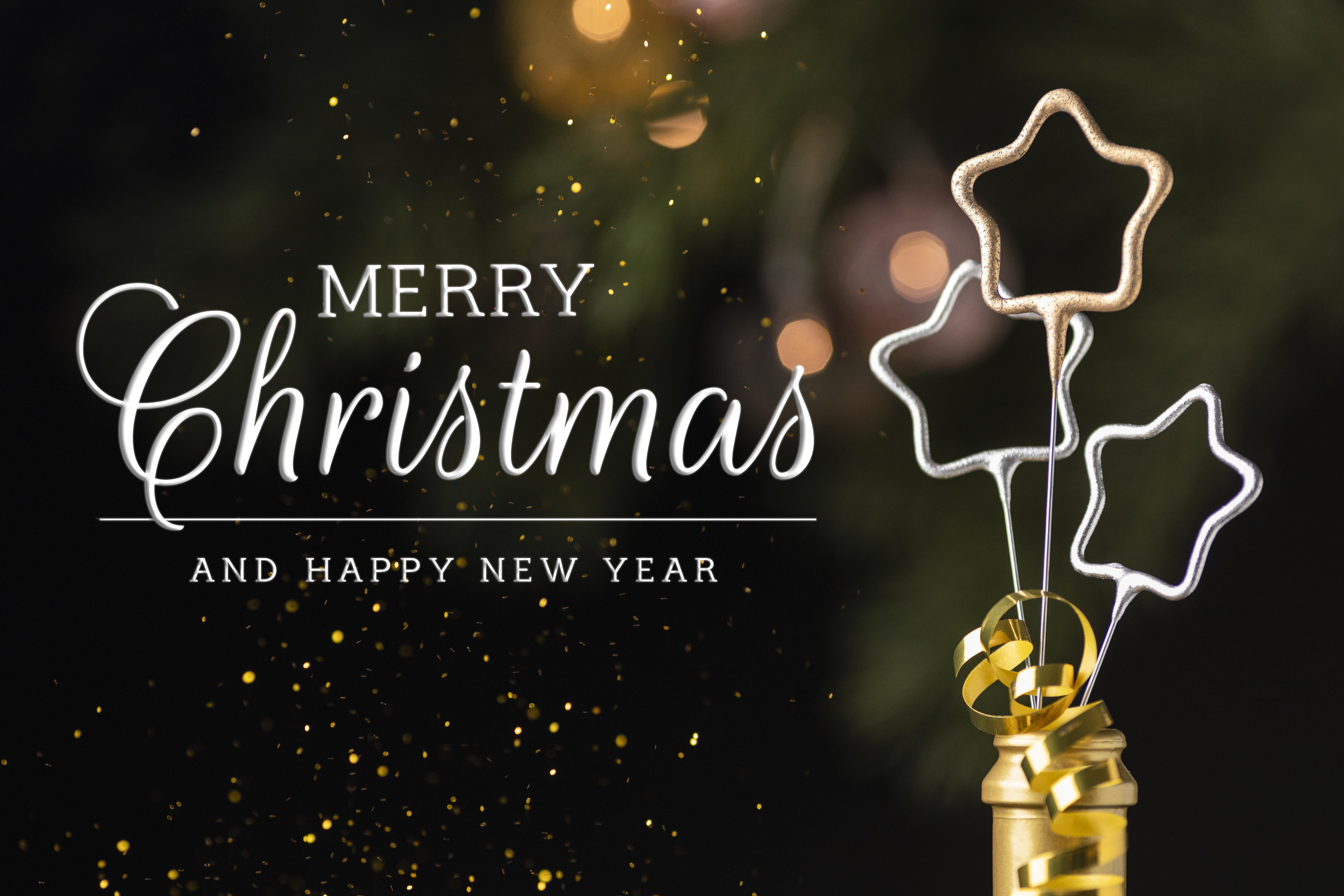 Schriftzug MERRY Christmas AND A HAPPY NEW YEAR neben Stern-Wunderkerzen und Glitzerstaub im Hintergrund