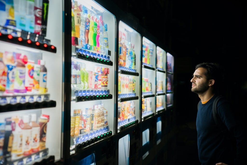 Ein Mann steht vor fünf Kühlschränken, in denen farbige Getränke stehen